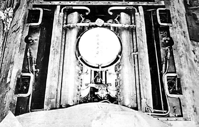 Вид на двигатель танка Т-34 со стороны башни. За «блином» воздухоочистителя виден заливной тройник  с паровоздушным клапаном, предназначенный для заливки воды в систему охлаждения. По бортам, между шахтами подвески видны масляные баки.