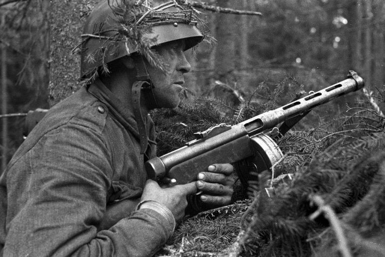 Финский солдат в лесу в засаде с пистолетом-пулеметом «Суоми» в руках.