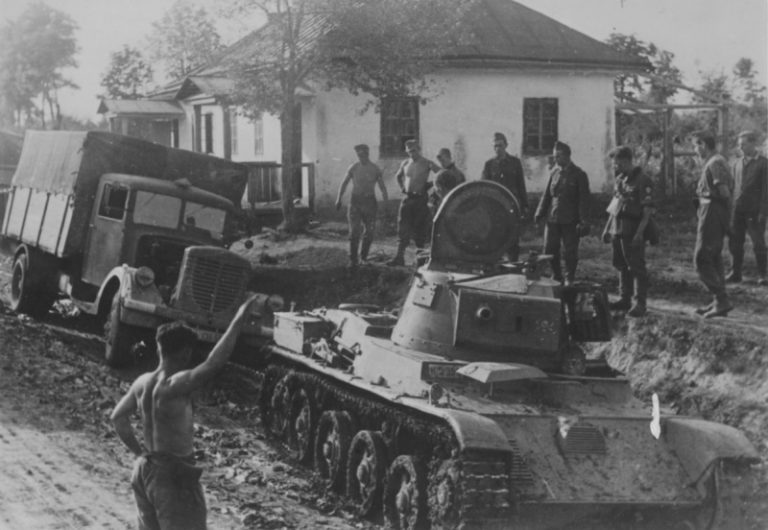 Венгерский танк 38M Toldi I со снятым вооружением буксирует немецкий грузовик Büssing-NAG 400 по улице советской деревни